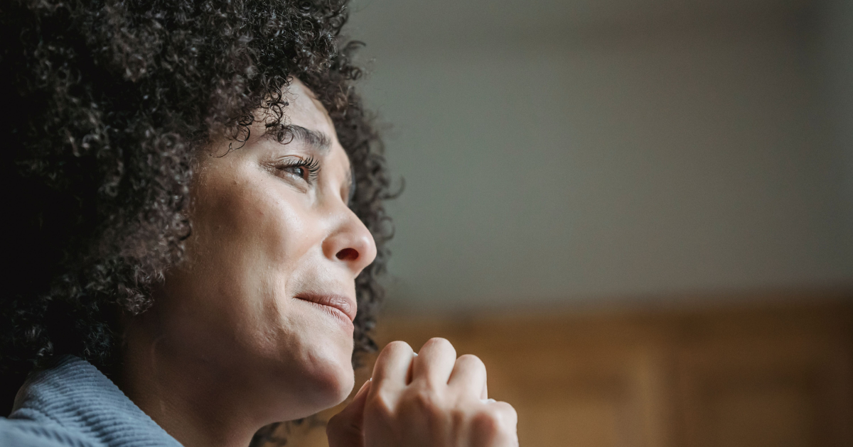 Close-up of a woman with curly hair gazing upward with a thoughtful expression.