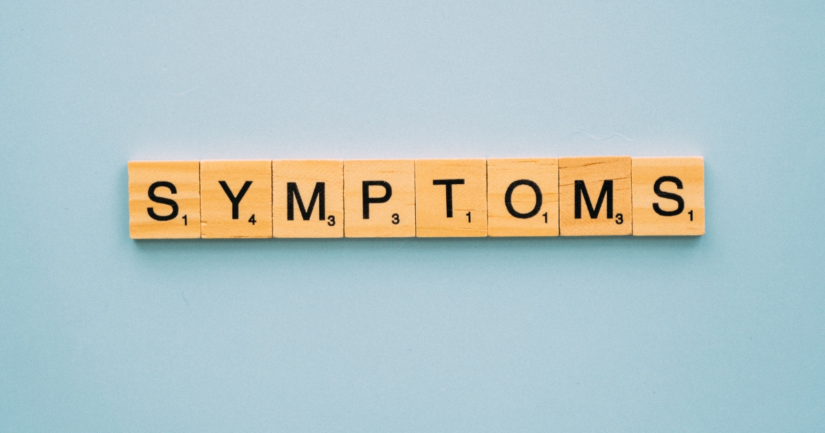 Wooden letter tiles on a blue background spell the word 'SYMPTOMS'.