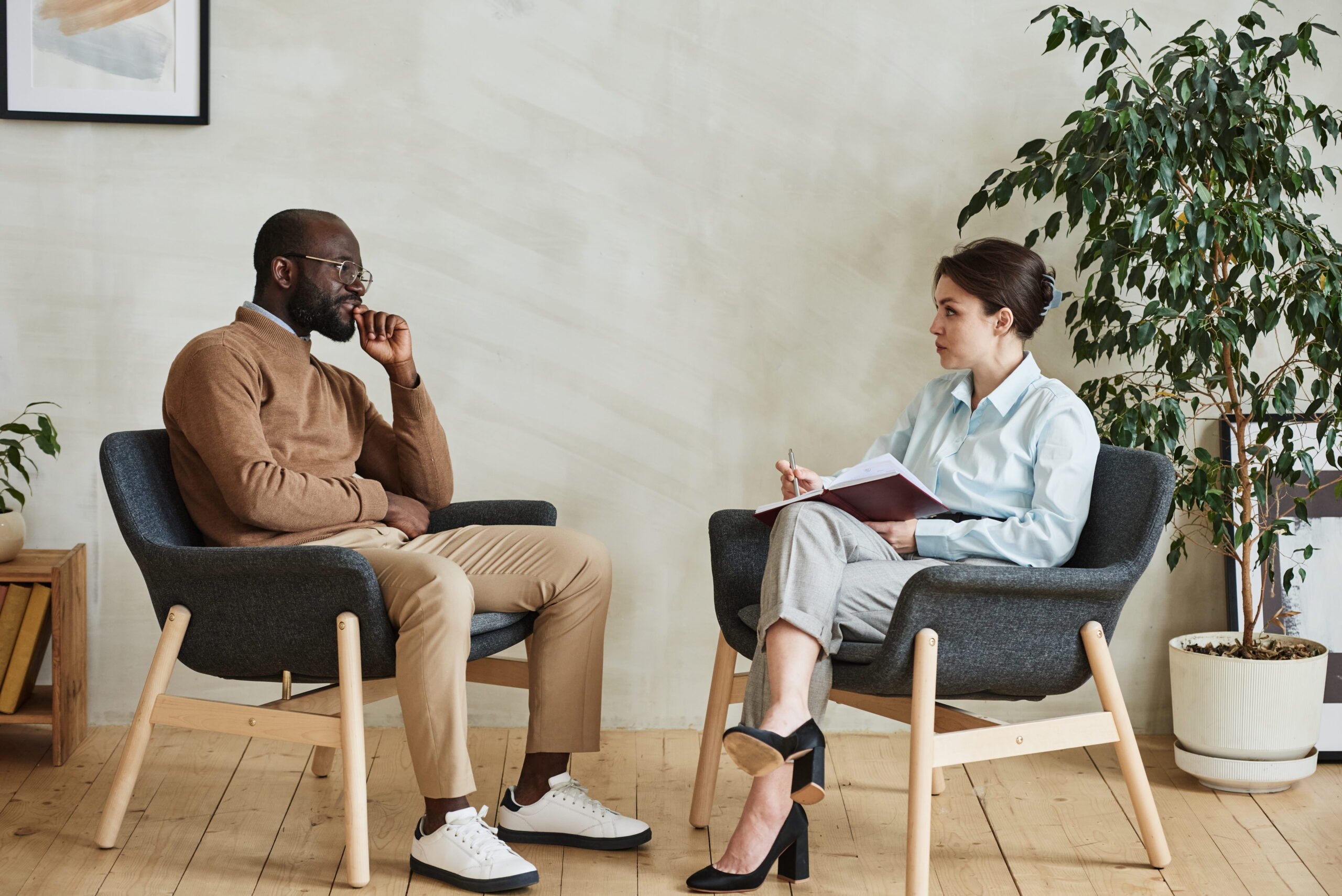 Two people sit in armchairs facing each other in a calm office, a counseling session or interview is taking place.